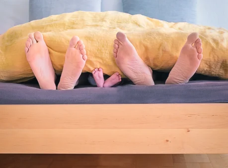 Family relaxing on a bed with feet uncovered.